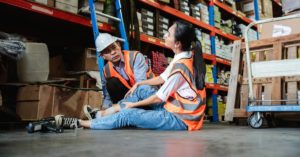 male warehouse supervisor helping female employee who has suffered leg injury on the job