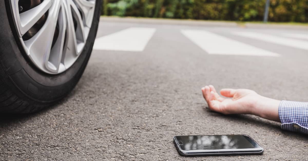 male pedestrian lying injured in the road next to his phone after an accident