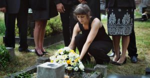 grieving woman surrounded by family placing flowers on a loved one's grave
