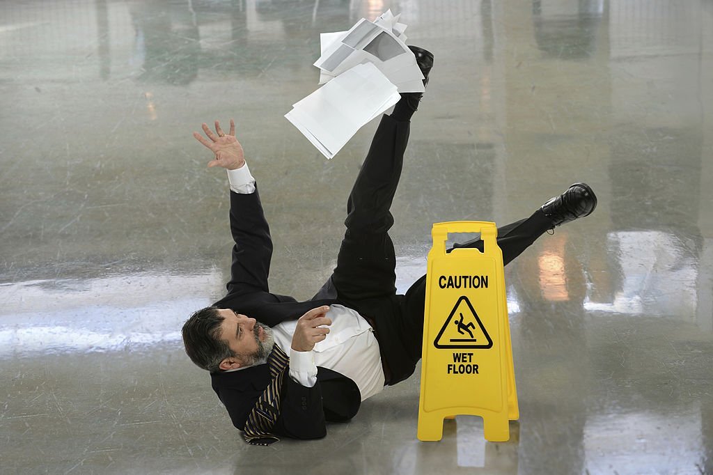 Senior Man Falling on a Wet Floor in Front of Caution Sign