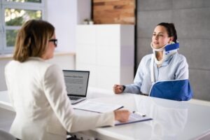 Worker with her left arm in a sling and wearing a neck brace meeting with their supervisor to discuss who pays their health insurance while on workers’ compensation